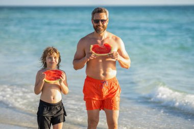 Baba ve oğlu sahilde. Sevgi dolu baba ve oğul denizde güzel vakit geçiriyorlar. Babalar Günü konsepti. Baba oğul karpuz yiyorlar. Baba ve oğul yaz tatilinde..