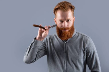 Gri arka planda berber bıçağıyla tıraş olan bir adam, kopyalama alanı. Berber adam bıçakla tıraş oluyor. Berber stüdyosundaki adam. Adam tıraş olmak için berber bıçağını tutuyor..