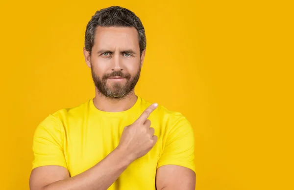 stock image positive man pointing at advertisement offer isolated on yellow. man pointing at advertisement offer on background. man pointing at advertisement offer in studio. man pointing at advertisement offer.