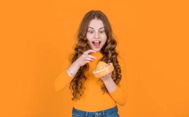 amazed teen girl hold orange and juicer on yellow background.