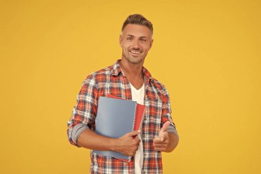 Okul kitaplarını sarı arka planda tutan gündelik parmakla işaret eden mutlu adam, öğrenci..