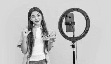 Tacını işaret eden genç blogcu kız sarıda izole edilmiş. Stüdyoda taç giyen genç blogcu kız. Geçmişinde taç olan genç blogger kız. Taçlı genç blogcu kızın fotoğrafı.