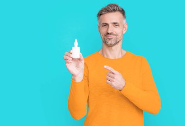 man hold nasal medicine on background, point finger. photo of man hold nasal medicine. man hold nasal medicine isolated on blue. man hold nasal medicine in studio.