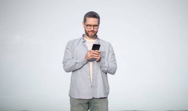 smiling man in glasses chat on smartphone with message. man chatting on phone messaging. smartphone communication. man chat on sky background.