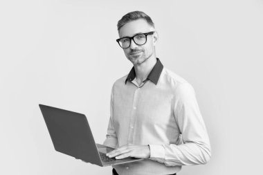 Gözlüklü olgun yönetmen gri arka planda bilgisayar üzerinde çalışıyor..