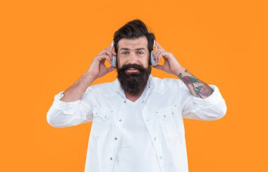 Gülümseyen hippi adam sarı arka planda izole edilmiş kulaklıklarla dinleme defteri. Kulaklıkla kitap. Dinleme kitabı için kulaklık takan bir adam. Müzik dinlemek için kulaklık tutan hipster 'ın stüdyo fotoğrafı..