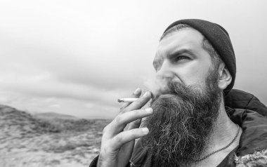 caucasian bearded man smoking cigarette. photo of man smoking cigarette in the mountain. man smoking cigarette outdoor. man with beard smoking cigarette.