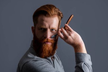 Bıçaklı yakışıklı kuaför. Kuaför stüdyosundaki adam. Saç kesimi için kuaför bıçağını tutan adam. Erkek saç kesimi kavramı. Erkek kuaför gri arka planda saç kesimi yapar..