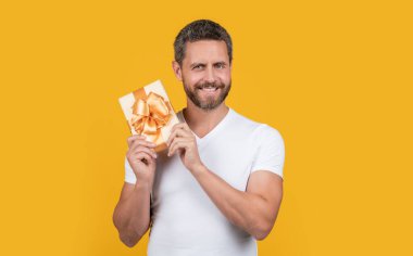 Mutlu adam hediye kutusunu stüdyoda tutuyor. Tatil için hediye kutusu olan bir adam. Bir adamın hediye kutusunun fotoğrafı. Adam mevcut kutuyu sarı arkaplanda izole olarak tutuyor.