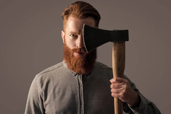 髭を生やした残忍な男は灰色の背景で隔離された斧を持っている 斧を持つ残忍な男は髭を生やしている スタジオで撮影された赤いひげの残忍な男 — ストック写真