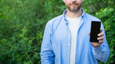 Akıllı telefon ekranını fotokopi aletiyle sunan adamın kırpılmış görüntüsü. Akıllı telefon sunan adamın fotoğrafı. Akıllı telefon sunan adam. Adam dışarıda akıllı telefon sunuyor..