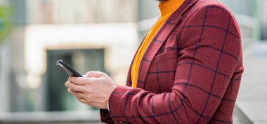 Sokakta akıllı telefondan mesajlaşan bir adamın görüntüsü. Dışarıda akıllı telefondan mesaj atan bir adam var. Akıllı telefondan ceketle mesaj atan adamın fotoğrafı. Adam açık havada akıllı telefondan mesaj atıyor..
