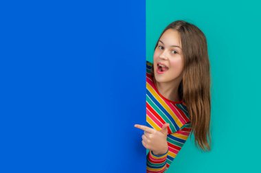 Reklam için fotokopi alanı olan boş mavi kağıdın arkasındaki hayret verici kız. işaret parmağı.