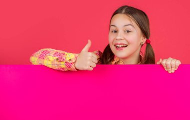 Reklam için fotokopi alanı olan boş pembe kağıdın arkasında mutlu bir çocuk. başparmak yukarı.