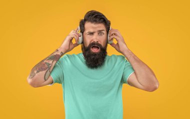 Sinirli adamın sarı kulaklıklarda yüksek sesli müziği var. Sinirli adam kulaklıkla yüksek sesle müzik dinler. Yüksek sesli kulaklıklı rahatsız bir adam. Yüksek sesli müzikle rahatsız bir adamın stüdyo çekimi..