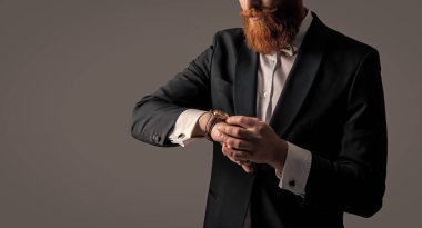 Smokin stüdyosunda çekilen dakik adam. Saati kontrol et, yeri kopyala. Saati ve smokini zamanında kontrol et. Smokinli dakik sakallı adam gri arka planda izole edilmiş saati kontrol et..