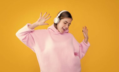 Neşeli genç kız sarı arka planda kulaklıkla müzik dinliyor..