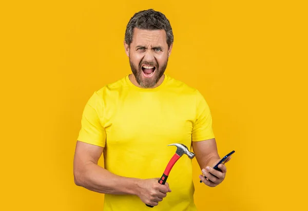stock image shouting man hack the phone in studio. photo of man hack the phone with hammer. man hack the phone isolated on yellow. man hack the phone on background.