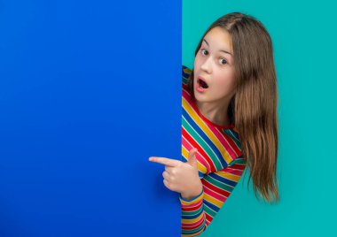 Boş mavi kağıdın arkasında reklam için fotokopi alanı olan sürpriz bir kız. işaret parmağı.