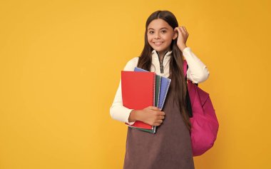 Okul çantası ve sarı arka planda not defteri olan mutlu bir çocuk..