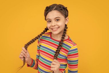 photo of cheerful teen girl having braids. childhood studio shot of teen girl has braids. teen girl with braids isolated on yellow background. teen girl with braids on hair in studio. clipart