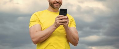 Gökyüzü arka planında akıllı telefondan konuşan bir adamın görüntüsü.