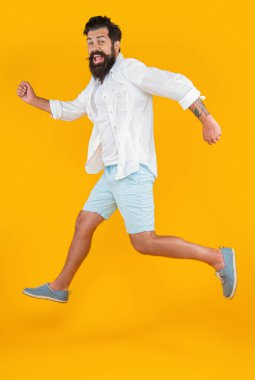 Stüdyoda aceleci sakallı adam. Sakallı adam arka planda acele ediyor. Sakallı adamın yaz modası giydiği bir fotoğraf. Acele eden sakallı adam sarıda tek başına..
