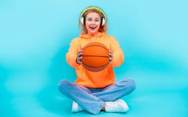 Basketbolcu kadının seçici odak noktası stüdyoda müzik dinlemek. Basketbolcu kadın arka planda müzik dinliyor. Basketbolcu kadının fotoğrafı müziği sever. Basketbolcu kadın mavi üzerine izole edilmiş müziği sever..