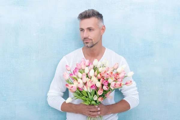 stock image photo of man with valentine flowers for holiday. man with valentine flowers. man with valentine flowers in studio. man with valentine flowers isolated on blue backdrop.