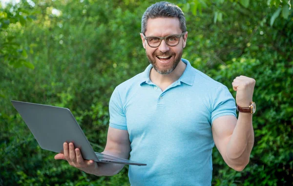 stock image glad programmer man online outdoor. programmer man working online on laptop. photo of programmer man online on computer. programmer man online.