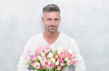 cheerful man with spring tulips in studio. man with spring tulips isolated on blue background. photo of man with spring tulips. man with spring tulips.