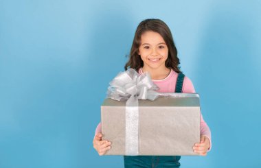 glad girl with birthday gift in studio. girl with birthday gift on background. photo of girl with birthday gift box. girl with birthday gift isolated on blue.