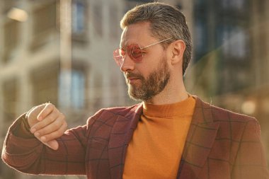 punctual man check time on wristlet watch outside. photo of punctual man check time on watch. punctual man in jacket check time outdoor. punctual man check time in the street.