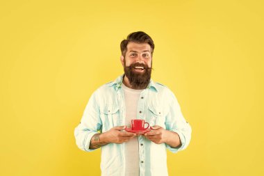 Mutlu sakallı adam sabah kahvesini içiyor sarı arka planda başparmağını gösteriyor, sabah.