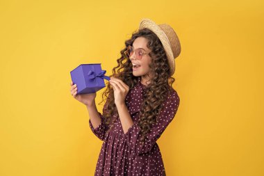 surprised kid with curly hair hold present box on yellow background.