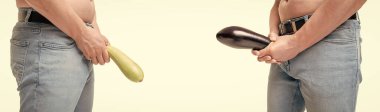 Men crop view holding eggplant and zucchini imitating erect penis and limp-dick isolated on white.