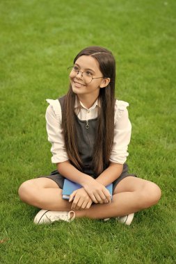 Happy teenage school girl sitting legs crossed on grass. School and education. Back to school.