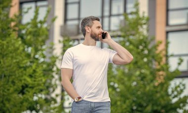 Yetişkin bir adamın dışarıda telefonu var. Sokakta telefonla konuşan bir adam var. Dışarıdaki adam aradı. Bir adamın telefon edip konuştuğu bir fotoğraf..