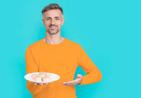 stock image man hold yummy macaroon in studio, presenting. man hold yummy macaroon on background. photo of man hold yummy macaroon. man hold yummy macaroon isolated on blue.