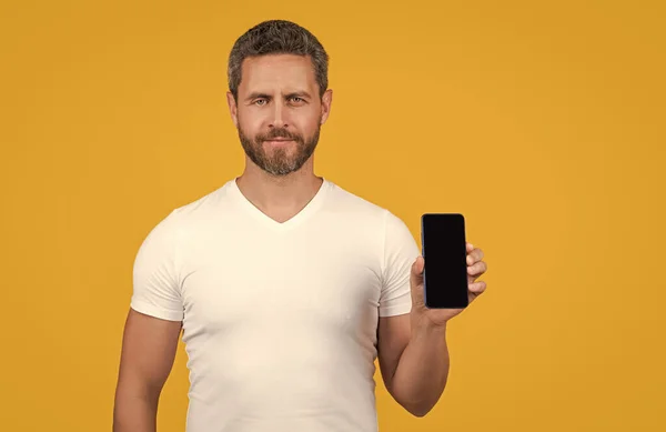 stock image man showing phone screen isolated on yellow background. man showing phone screen in studio. man showing screen of phone. man showing phone screen with copy space.