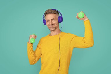 Stüdyoda müzik kulaklığı takan mutlu fitness adamı. Arka planda müzik kulaklığı takan fitness adamı. Müzik kulaklığı takan fitness oyuncusunun fotoğrafı. Müzik kulaklıklı fitness adamı mavi renkte izole edilmiş..