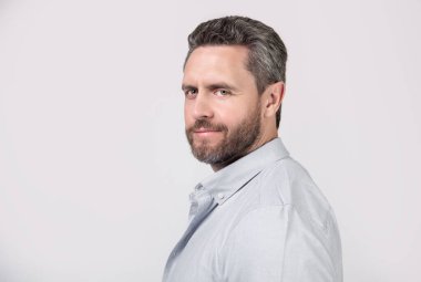 Stüdyoda sakallı, olgun bir adamın portresi. Sakallı, olgun bir adamın fotoğrafı. Kirli sakallı, normal gömlekli olgun bir adam. Gri arka planda sakallı, olgun bir adam..