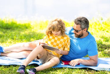 Baba ve oğul parkta dinleniyor. çocukluk okulu eğitimi. Oğlu ve babası yazın kaynaşıyorlar. Baba ve oğul eğitimi almış. Baba oğul eğitimini kitap ve tabletle şekillendirir. aile eğitimi.