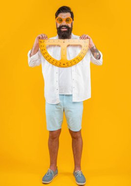 Pozitif adam geometri açısını sarı üzerine izole etti. Stüdyoda geometri açıölçer var. Adam arka planda geometri açıölçer tutuyor. insan tutuşu geometri iletkeninin fotoğrafı.