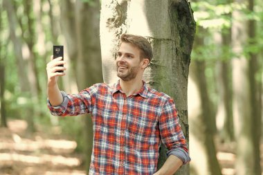 Gülümseyen adam blogcu akıllı telefondan selfie çekiyor. Blogcu adamın fotoğrafı ormanda selfie çekiyor. Blogcu adam dışarıda selfie çekiyor. Adam blogcu telefonda selfie çekiyor..