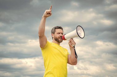 Sarı tişörtlü adam arka planda hoparlörle ajitasyon yapıyor..