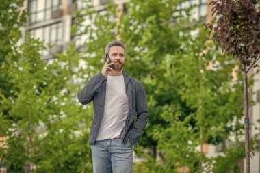Adamın açık havada akıllı telefon görüşmesi var. Sokakta akıllı telefon görüşmesi yapan bir adam. Adam dışarıdaki akıllı telefondan arıyor. Adamın fotoğrafı. Akıllı telefondan ara ve konuş..