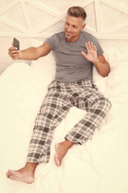 Yatakta telefonlu kameraman merhaba diyor. Evde telefonlu bir kameraman resmi var. Yatak odasında telefonlu bir adam var. Telefon eden adam pijama giyiyor..