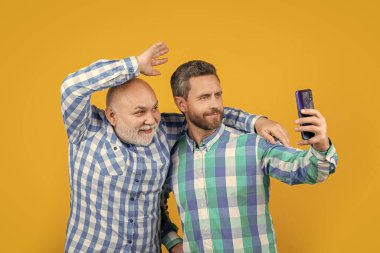 Mutlu kuşak erkeklerin telefonda selfie çektikleri bir fotoğraf. Nesiller boyu insanlar selfie 'yi sarıda izole ederler. Stüdyoda selfie çekiyorlar. Nesiller boyunca erkekler arka planda özçekim yaparlar..