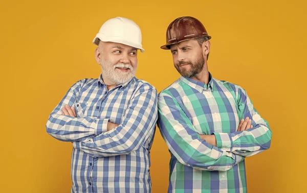 stock image cheerful workman generation men in studio. workman generation men on background. photo of workman generation men wear building helmet. workman generation men isolated on yellow.